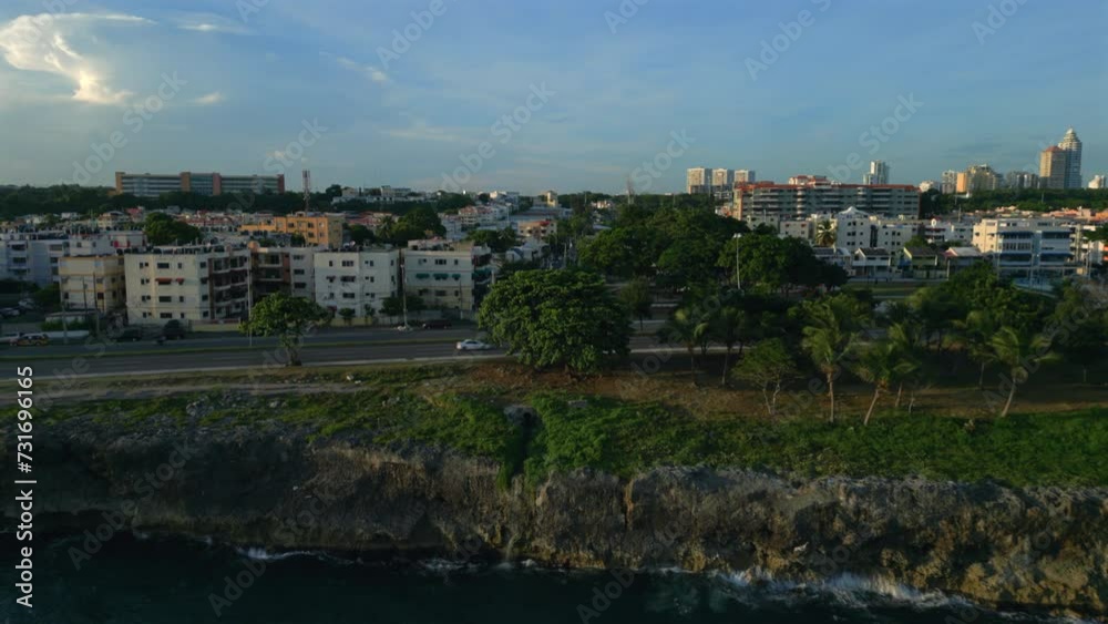 Drone shot of cars driving on a coastal road with seafront residential buildings in the background Drone shot of cars driving on a coastal road with seafront residential buildings in the background