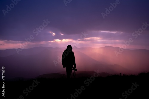 a person standing in a field at sunset with a silhouetted mountain