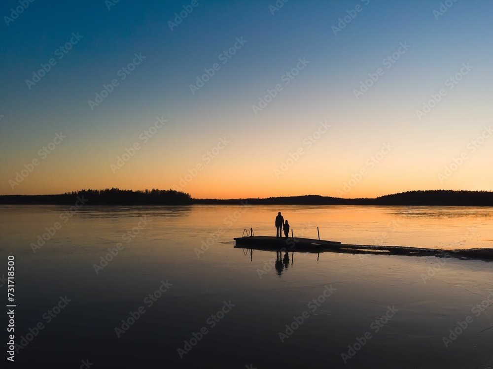 AI generated illustration of two people standing on a pier, silhouetted against sunset sky, Finland