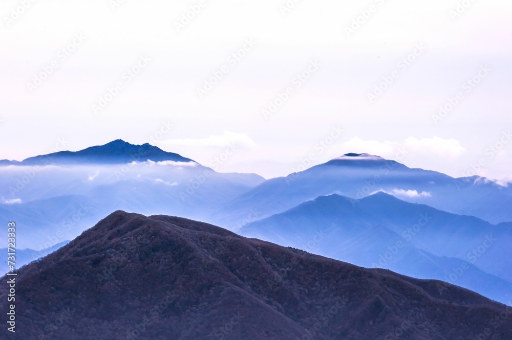 Picturesque landscape of a mountainous region shrouded in a light blue mist and low-lying clouds.
