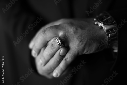 Greyscale close-up of an man's hands as he places his wedding ring on his finger © Wirestock