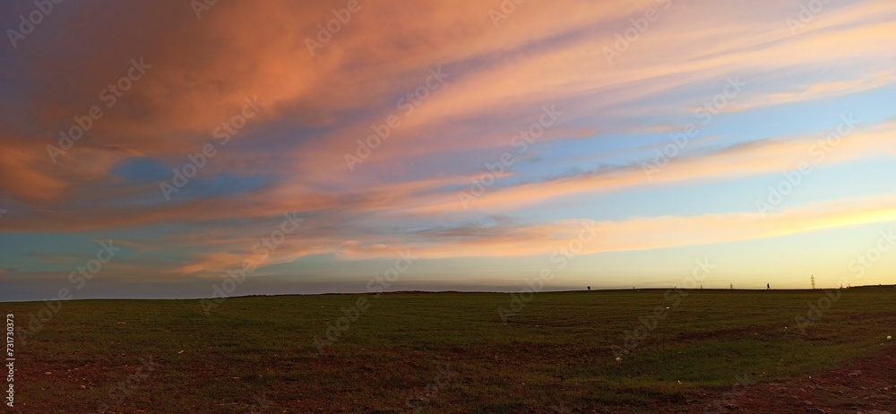Calm sky at sunset with large white clouds rolling in above a field of lush green grass