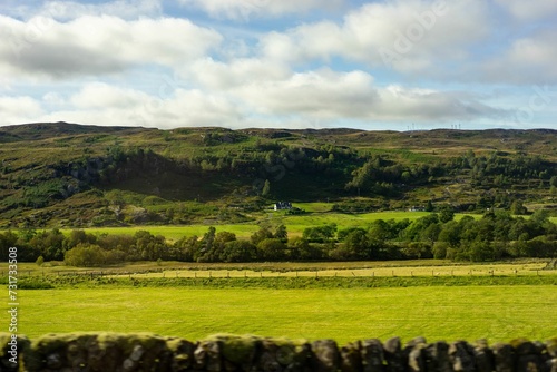 Scenic landscape view of Scotland featuring rolling grassy fields, lush green trees, and mountains