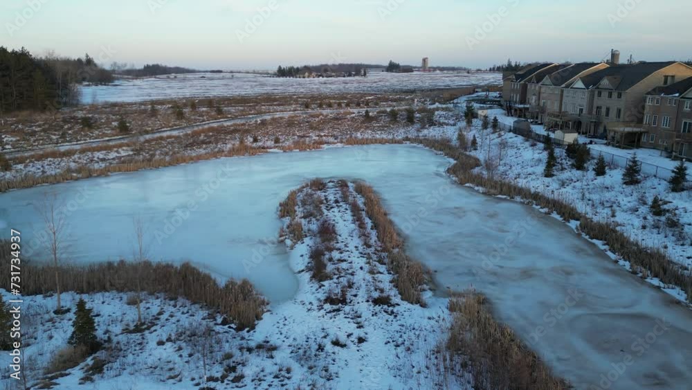 Aerial of a frozen lake surrounded by the winter forest and beautiful houses during the daytime Aerial of a frozen lake surrounded by the winter forest and beautiful houses during the daytime