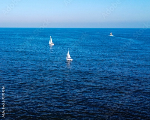 Sailboats are peacefully gliding on a tranquil, clear blue ocean under a bright sunny day