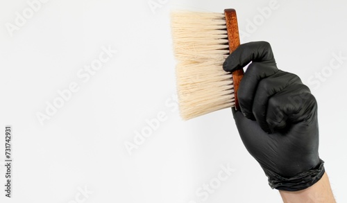 Hand in black gloves holding a brush with white synthetic bristles, isolated on a white background photo