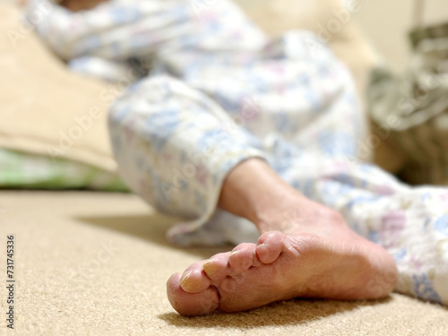 畳んだ布団の上に倒れている寝間着姿の高齢女性の足の裏