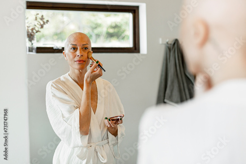 Reflection of woman suffering from cancer applying blusher on cheek in bathroom photo