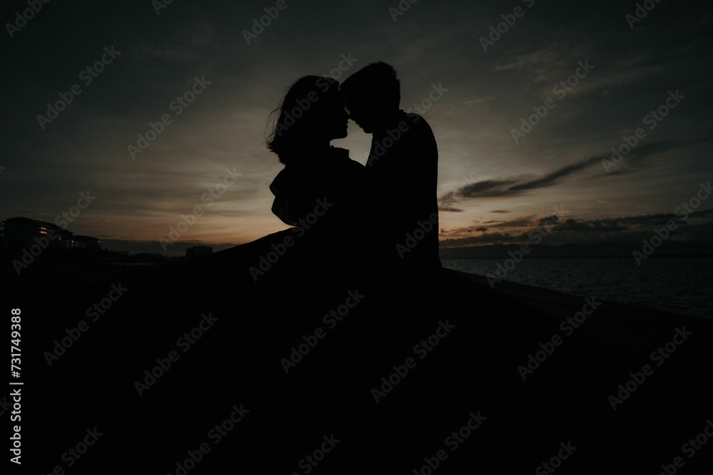 Silhouetted figures embracing in a romantic kiss against a beautiful sun-kissed dusky sky