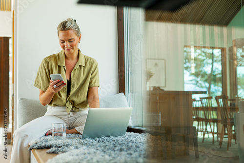 Smiling woman text messaging on smart phone while working at home photo