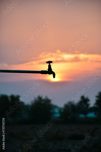 Closeup shot of a water tap against a backdrop of a deep orange-pink sunset.