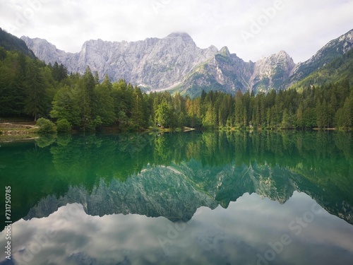 Green lake in the middle of a mountain range with some trees on each side © Wirestock