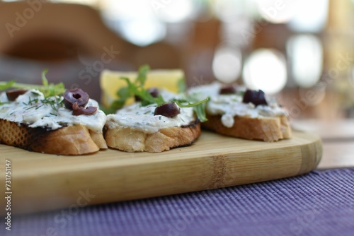 Close-up image of bruschetta with cream and olives arranged on a rustic wooden board