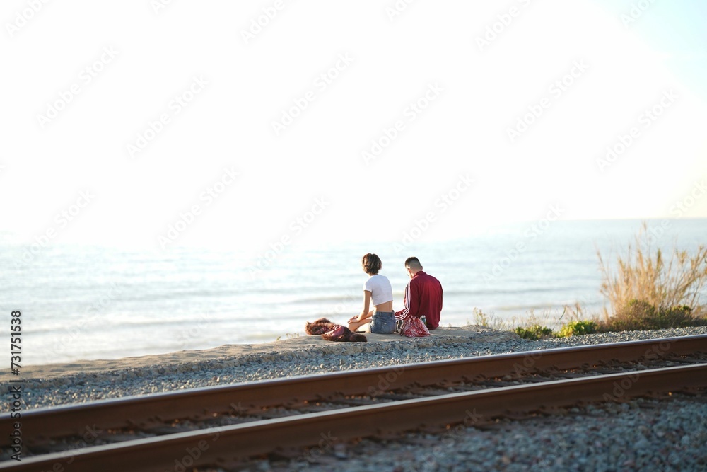 People seated side-by-side on a railroad track overlooking an ocean
