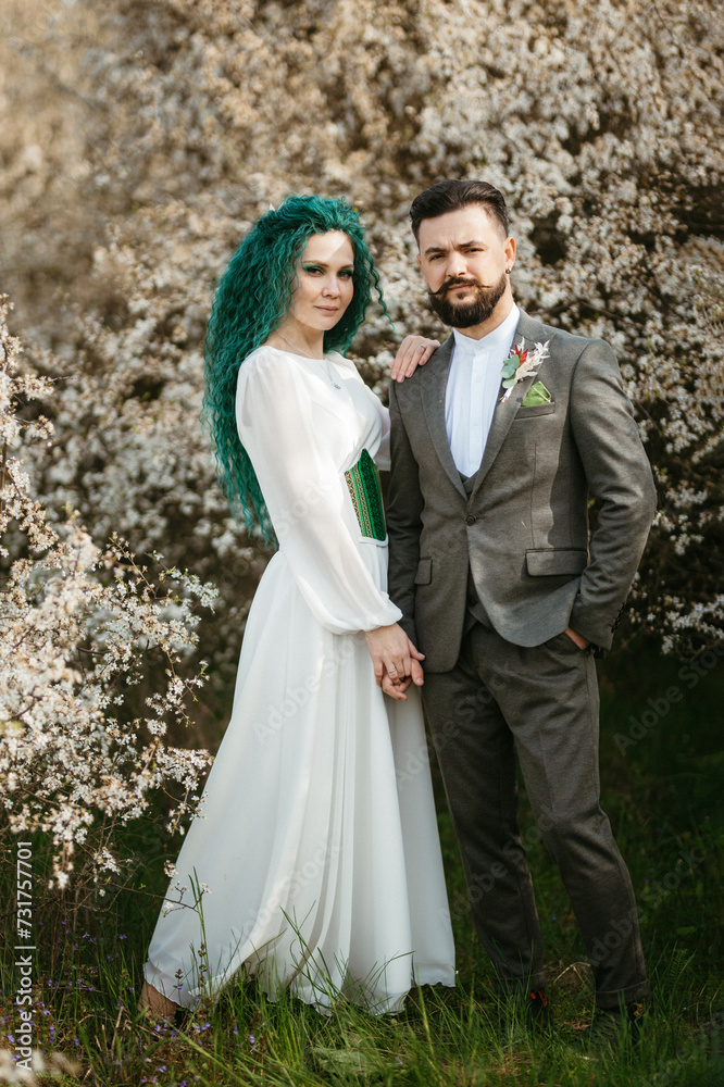 a bearded groom plays and a girl with green hair against the background of blooming spring