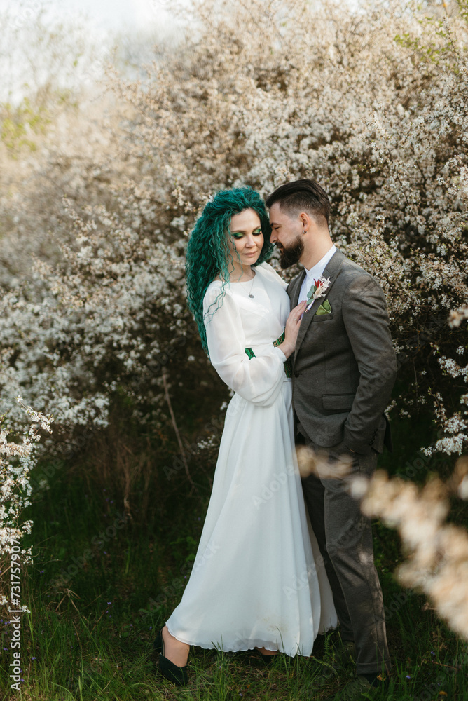 a bearded groom plays and a girl with green hair against the background of blooming spring
