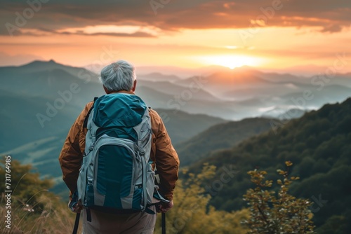 Close up back view of elderly mature man with a travel backpack on his back stands on mountain at sunset. Joyful free travel concept