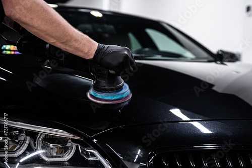 Car detailing worker polishing black car body with electric polisher photo
