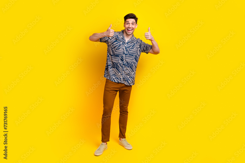 Full length photo of ecstatic satisified man dressed print shirt brown pants showing thumbs up approve isolated on yellow color background Full length photo of ecstatic satisified man dressed print shirt brown pants showing thumbs up approve isolated on yellow color background