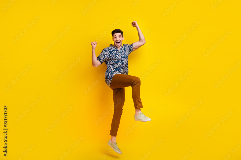 Full length photo of overjoyed man dressed print shirt brown trousers raising fists up win gambling isolated on yellow color background