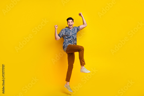 Full length photo of overjoyed man dressed print shirt brown trousers raising fists up win gambling isolated on yellow color background