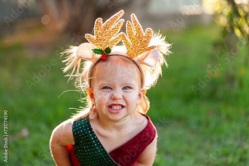 Happy smiling little girl in Christmas colours and wearing deer antler headband photo