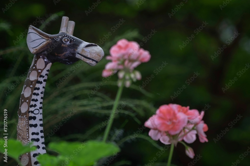 Fototapeta premium Garden figurine giraffe stands in a meadow of pink flowers