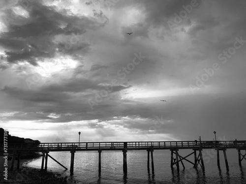 a cloudy sky over the water near a bridge and beach photo