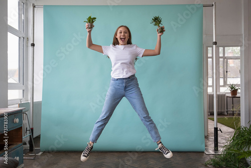 Studio portrait of teenage girl jumping with small potted plants in hands