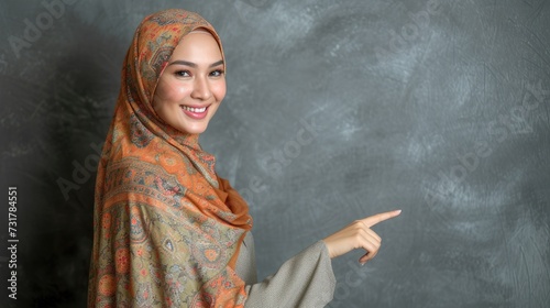 Beautiful young attractive woman in hijab pointing fingers up isolated over grey backround. Showing something with happy.