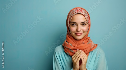 Portrait of beautiful young middle east woman in hijab smiling with a friendly expression closing her both hands isolated in blue background.