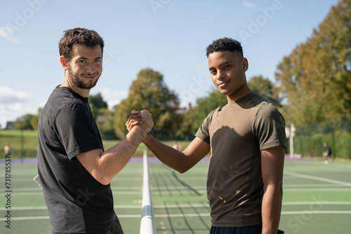 Portrait of two smiling men shaking hands in tennis court