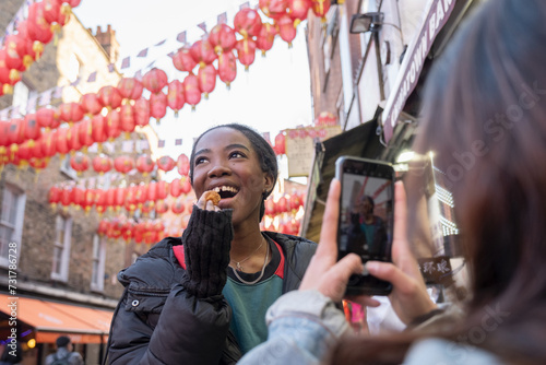 Canvas Print Young woman taking picture of friend eating taiyaki in Chinatown