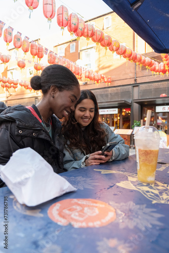 Young women checking phone while dining outdoors in Chinatown