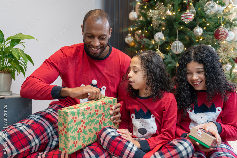 Obraz premium Smiling father with two daughters unpacking gifts in front of Christmas tree