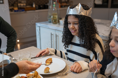 Smiling sisters in paper crowns at Christmas dinner table