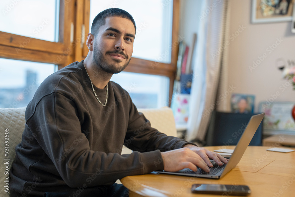Smiling young man working on laptop at home Smiling young man working on laptop at home