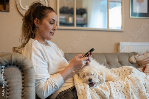 Woman with dog on sofa, using smartphone