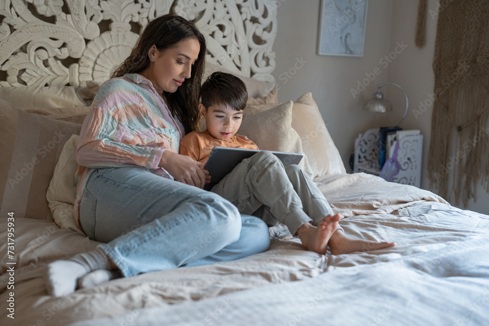 Fototapeta premium Mother and son (6-7) using digital tablet in bedroom