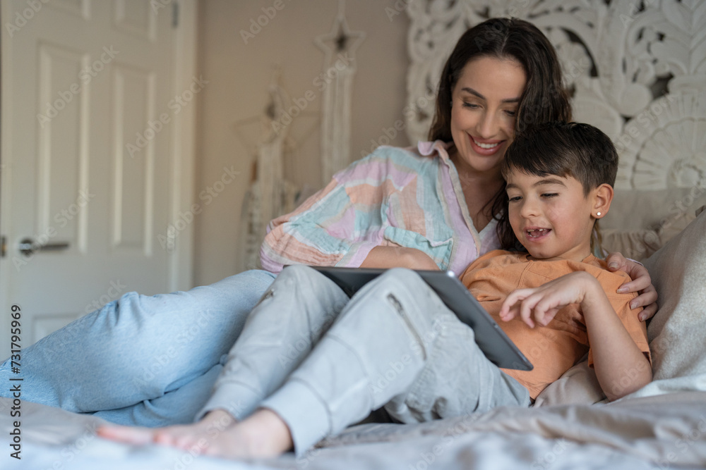 Mother and son (6-7) using digital tablet in bedroom