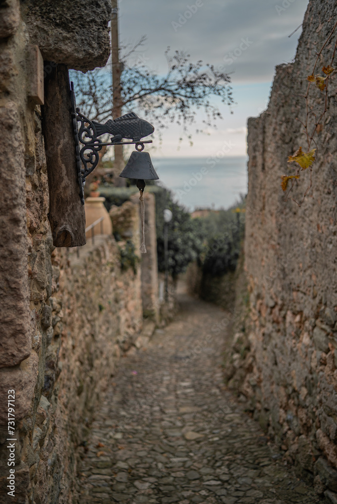 Vertical shot, a narrow, cozy medieval style street with a house ring as a bell and a beautiful sea on the background, Italy 