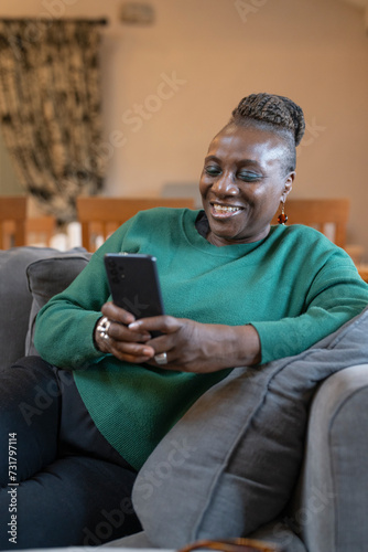 Smiling senior woman relaxing on sofa and using phone