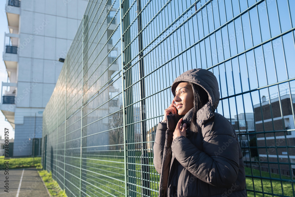 Φωτογραφία Portrait of smiling woman in overcoat with hood leaning at fence