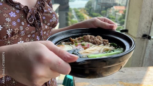 A girl carries hot soup in her hands Asian noodle soup, ramen with chicken, tofu, vegetables and egg in a black bowl. Slate background. Top view. photo