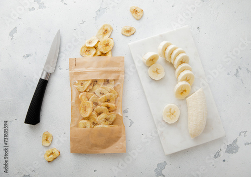 Pack of dried healthy bio banana chips with knife and raw banana.