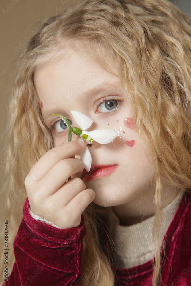 Portrait of cute little girl with glitters and red hearts on the face holding snowdrop flower Portrait of cute little girl with glitters and red hearts on the face holding snowdrop flower