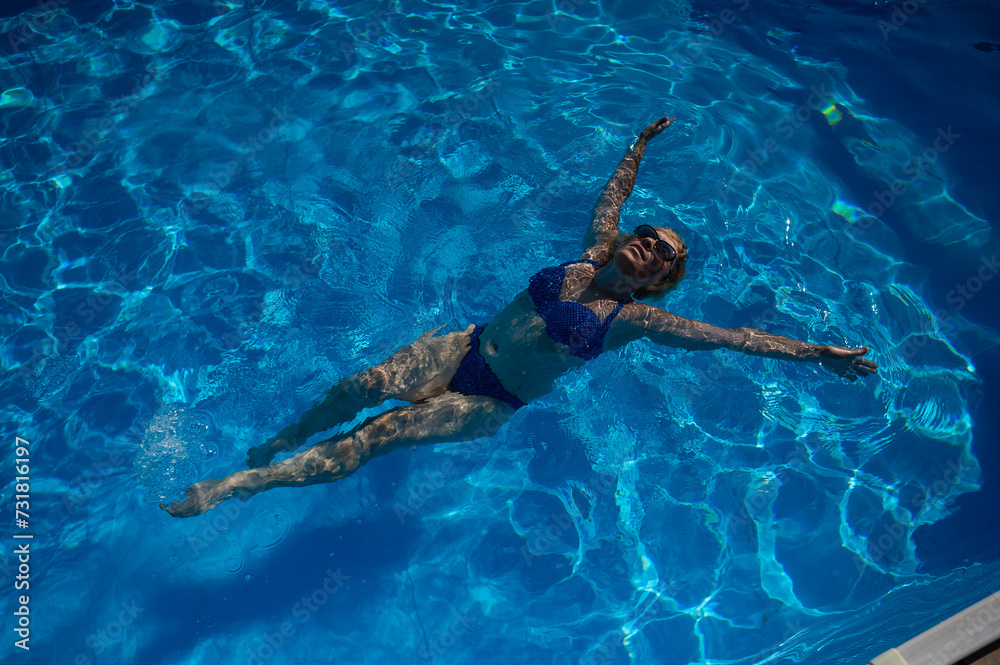 An elderly woman in sunglasses swims on her back in the pool. Vacation in retirement. 
