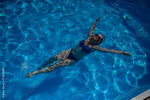An elderly woman in sunglasses swims on her back in the pool. Vacation in retirement. 