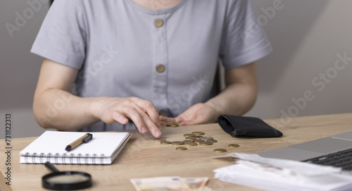 A woman sits at a wooden table and counts coins from her purse. . High quality photo