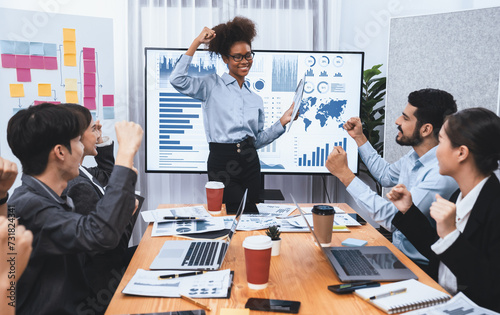 Business people celebrate after successful presentation or meeting on data analysis display on TV screen. Happy team gathers in office room, cheer to collaboration with celebratory gesture. Concord